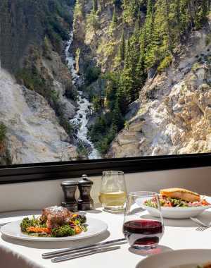 A table of food aboard the Rocky Mountaineer with a landscape view behind