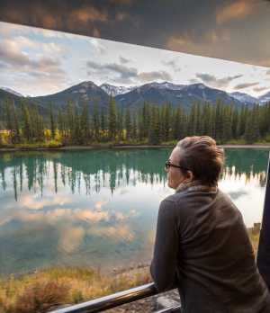 A lady gazes out of the Rocky Mountaineer at mountains and lakes
