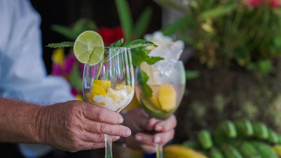 Liamuiga Natural Farms | A man's hand serves two glasses filled with mango, lime and ice at Liamuiga Natural Farms