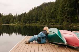 A woman relaxes on a dock in the Smash + Tess X MEC Fresh Air Fleece Jumpsuit
