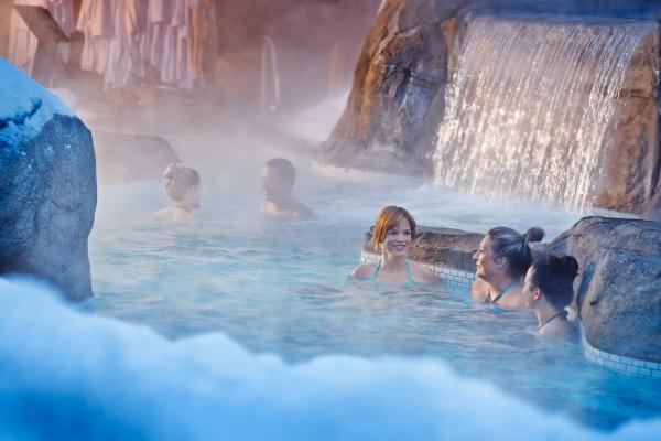 Nordik Spa-Nature - Chelsea, Quebec | People in an outdoor pool with a waterfall at Nordik Spa-Nature - Chelsea