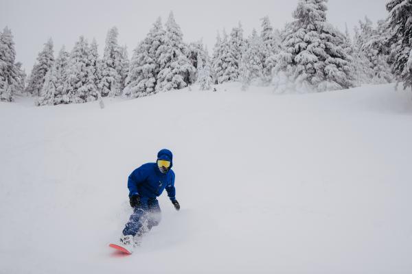 A snowboarder in a powdery terrain wearing the Men's Burton [ak] Swash GORE‑TEX 2L snowboarding jacket