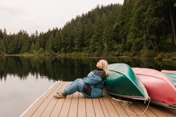 A woman relaxes on a dock in the Smash + Tess X MEC Fresh Air Fleece Jumpsuit A woman relaxes on a dock in the Smash + Tess X MEC Fresh Air Fleece Jumpsuit