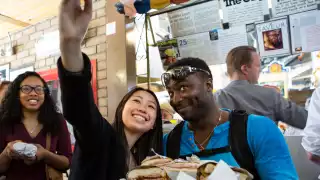 Kimpton Saint George | Two people on a food tour taking a selfie, holding a tray full of sandwiches
