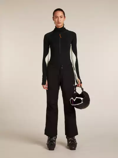 A woman wearing the icebreaker Merino 200 Oasis+ Thermal Suit with snowpants and ski boots