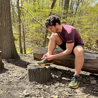 A person tying his shoes in the forest, sitting on a tree