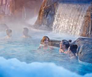 Nordik Spa-Nature - Chelsea, Quebec | People in an outdoor pool with a waterfall at Nordik Spa-Nature - Chelsea